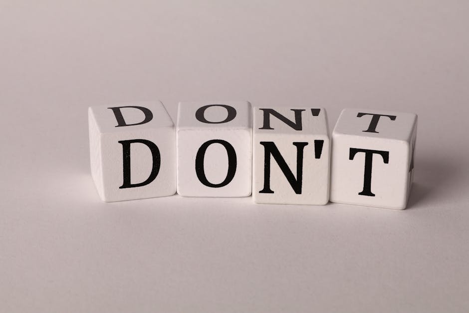 Four white cubic blocks with black lettering arranged in a row on a plain surface. The first block on the left displays the word 'DONT,' the second block reveals 'D,' the third shows 'ON,' and the fourth shows 'T,' forming the phrase 'DON'T DONT.' In the context of house removals and relocating services, the blocks symbolize caution or instructions related to moving processes. The background is neutral, and the lighting is soft, emphasizing the blocks and their message. The image is relevant to the topic of packing, loading, or moving logistics often handled by services like Man with Van Morden, facilitating home relocation or furniture transport.
